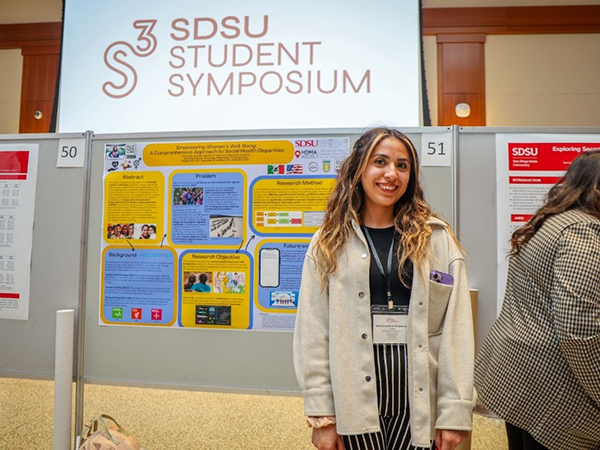 female student stands in front of poster presentation at S3 conference